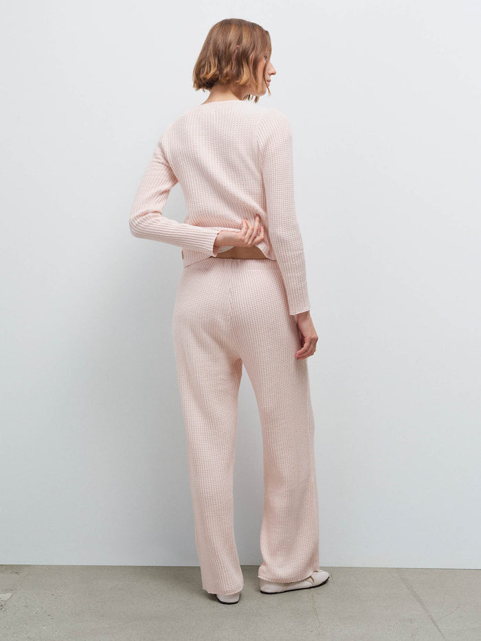 Woman standing wearing a pale pink waffle-knit cardigan and matching pants, back view in studio