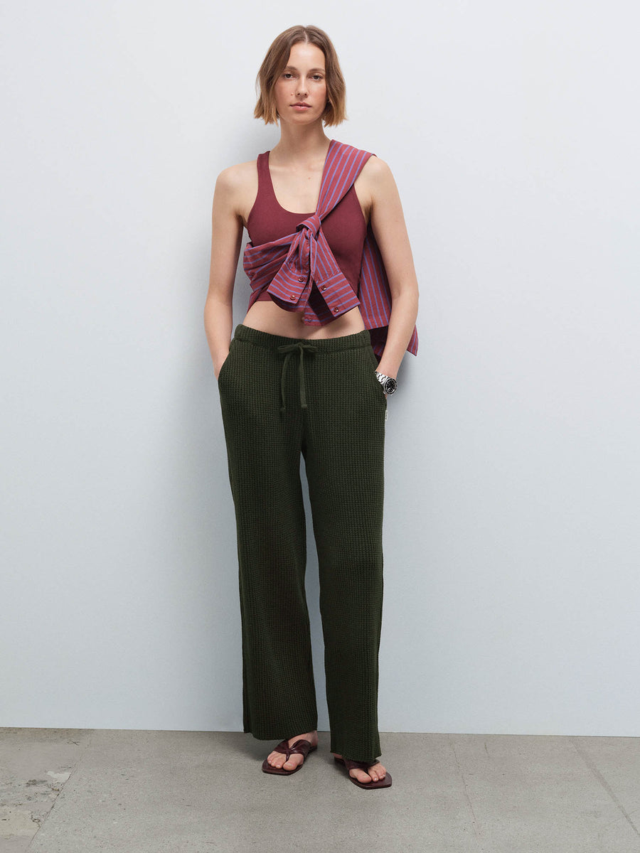 Woman wearing a burgundy racerback tank with a striped shirt tied at the waist and olive green waffle-knit wide-leg pants