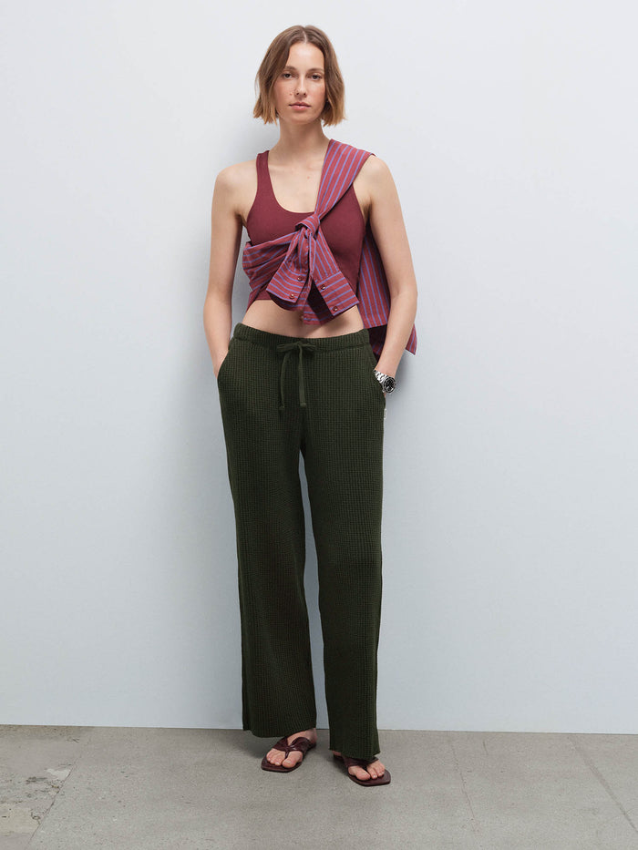 Woman wearing a burgundy racerback tank with a striped shirt tied at the waist and olive green waffle-knit wide-leg pants