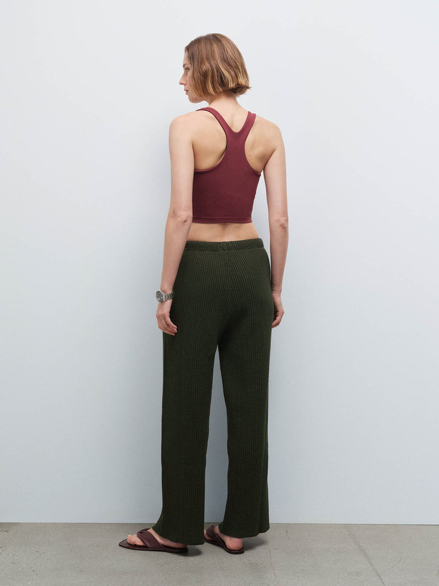 Woman wearing a burgundy racerback tank and olive green waffle-knit pants, back view in studio