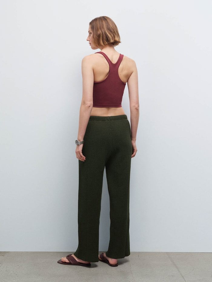 Woman wearing a burgundy racerback tank and olive green waffle-knit pants, back view in studio