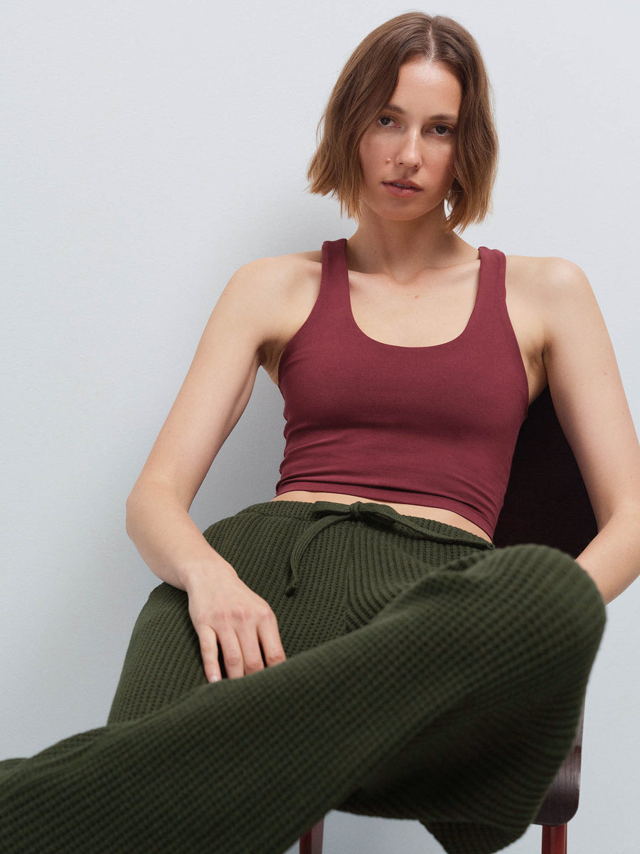 Woman seated in a chair wearing a burgundy racerback tank and olive green waffle-knit wide-leg pants