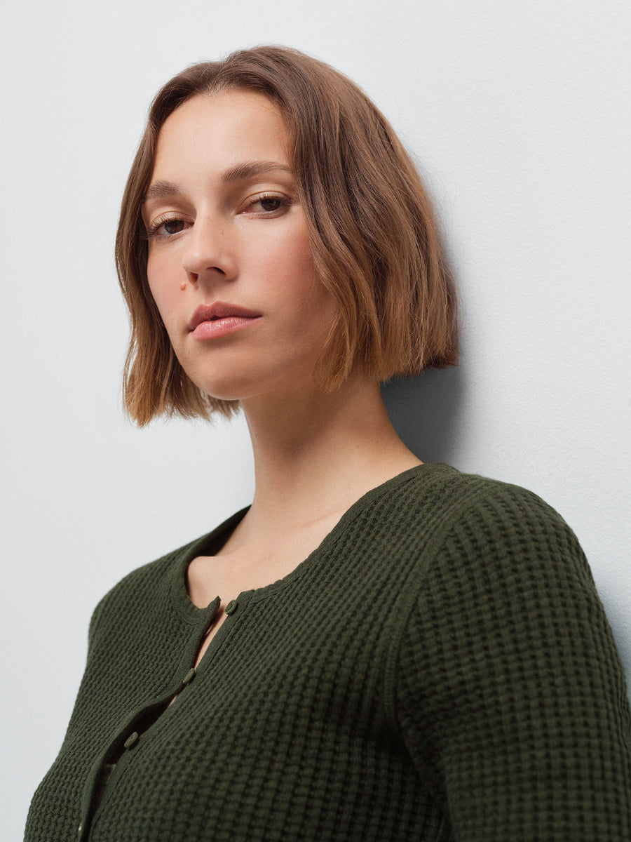 Close-up side profile of a woman's face and shoulder wearing an olive green waffle-knit cardigan