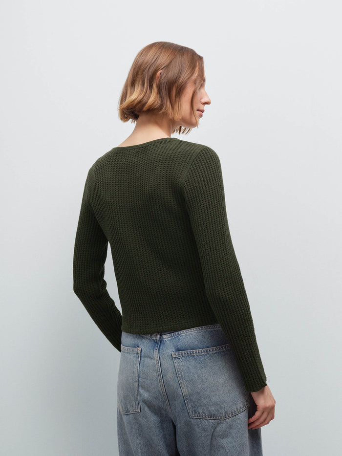 Woman wearing an olive green waffle-knit cardigan and denim jeans, back view showing knit texture in studio
