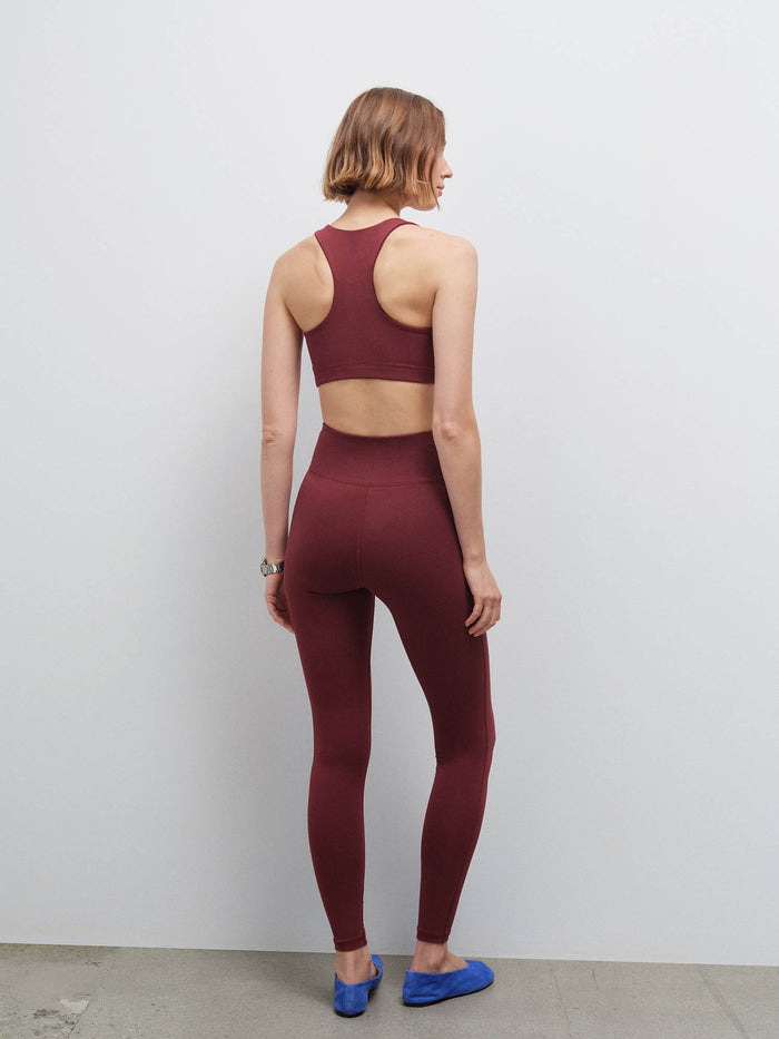 Woman standing wearing a burgundy racerback sports bra and matching leggings, back view with blue flats