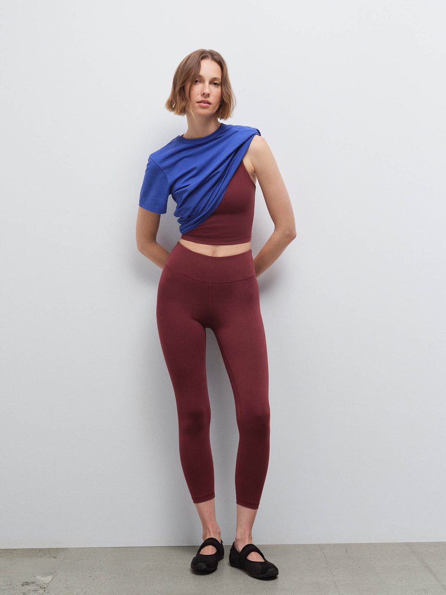 Woman wearing mulberry midi leggings and cropped top with blue shirt draped over shoulder, front view in studio