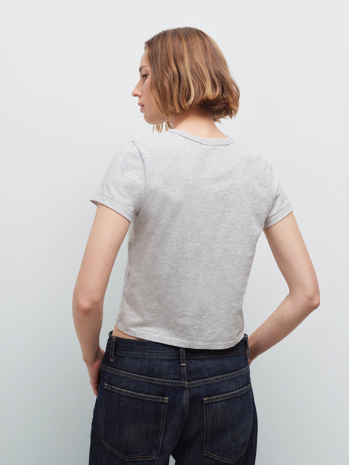 Woman wearing a light heather gray cropped tee and dark denim jeans, back view in studio