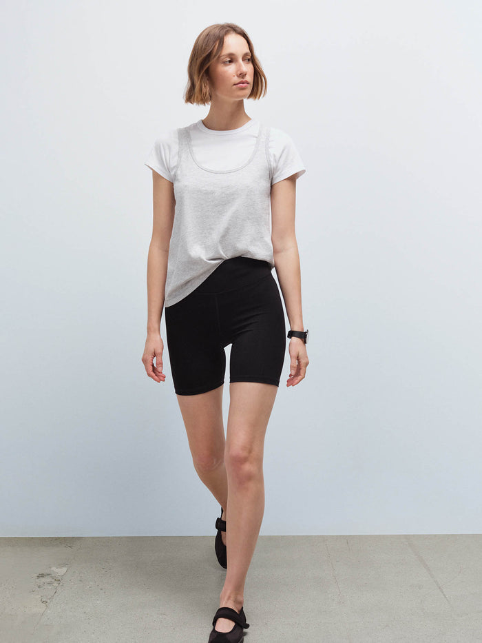 Woman walking wearing a white tank layered over a heather grey tank with black biker shorts