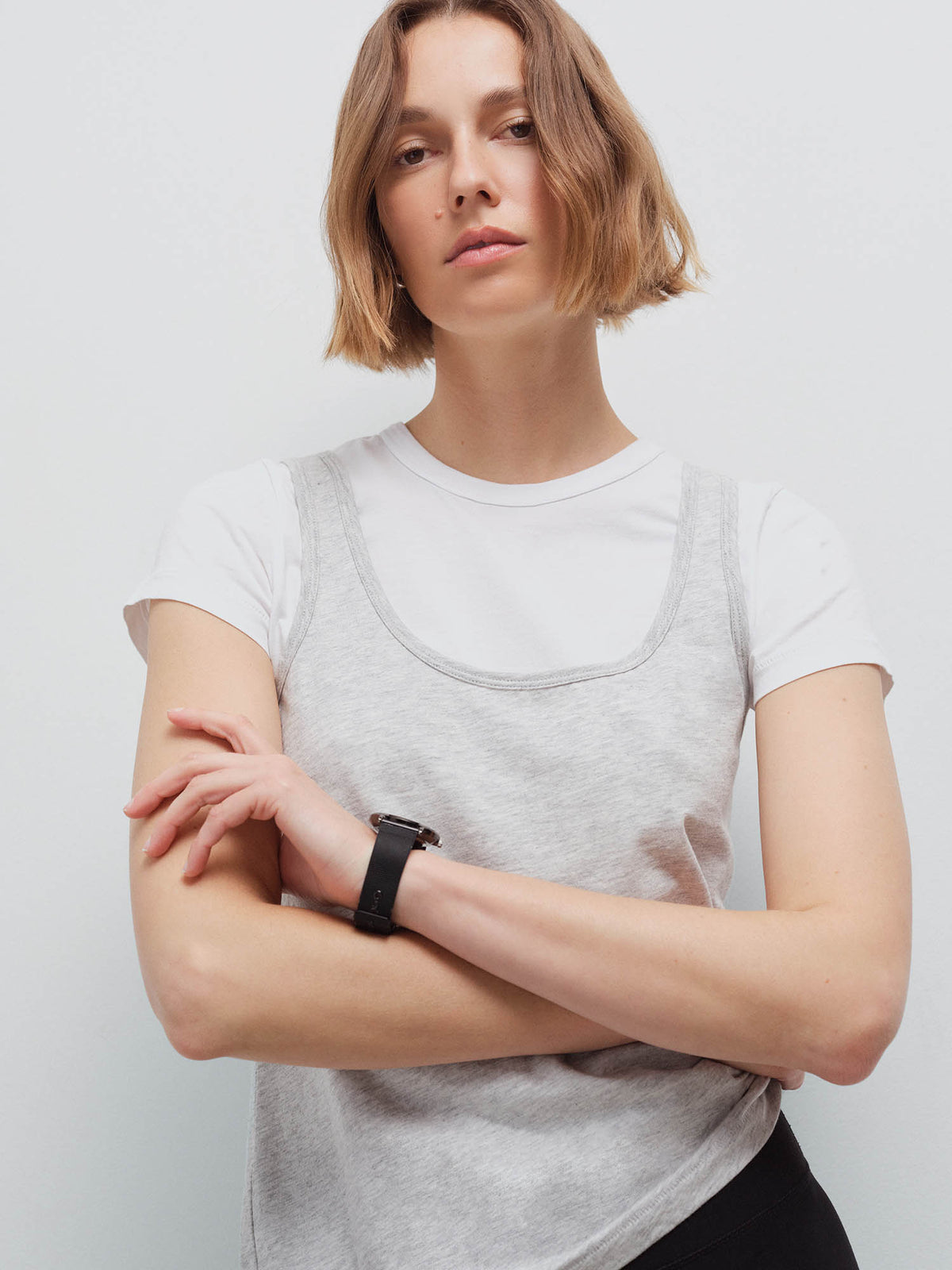 Close-up of a woman with arms crossed wearing a heather grey tank layered over a white tee