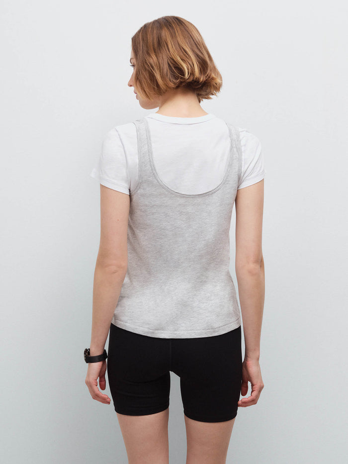 Woman standing wearing a heather grey tank layered over a white tee and black biker shorts, back view