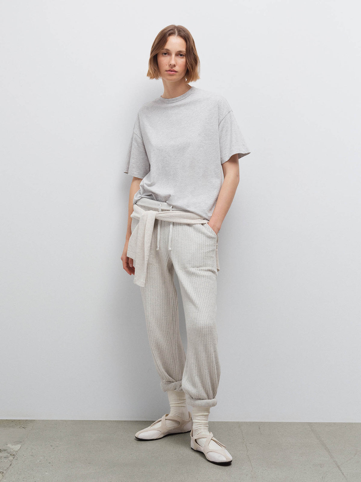 Woman wearing heather grey oversized pima tee and cream sweatpants with a sweater tied at waist, studio