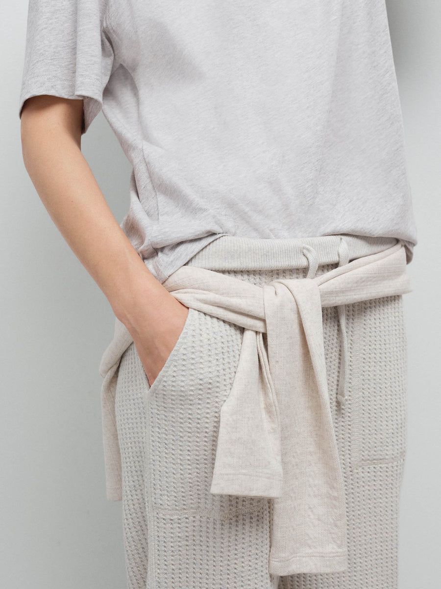 Detail shot of a sweater tied at the waist over cream waffle-knit sweatpants, close-up in studio