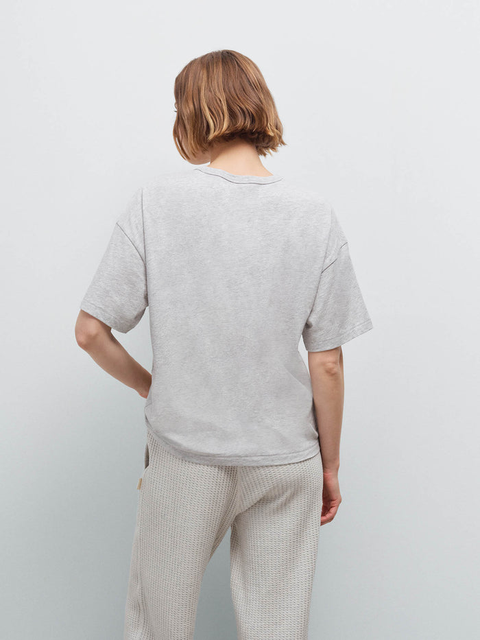 Woman wearing heather grey oversized pima tee, back view showing relaxed drop-shoulder fit in studio