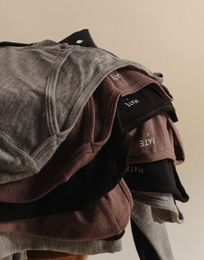 Close-up of folded MATE merino wool tops in grey, peppercorn brown, and heather grey stacked together