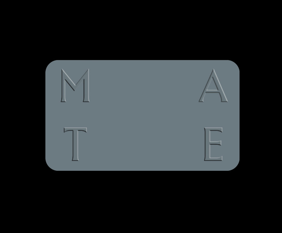 A rectangular slate gray plaque with rounded corners, featuring the embossed letters 'M', 'A', 'T', and 'E' arranged in a 2x2 grid on a solid black background.