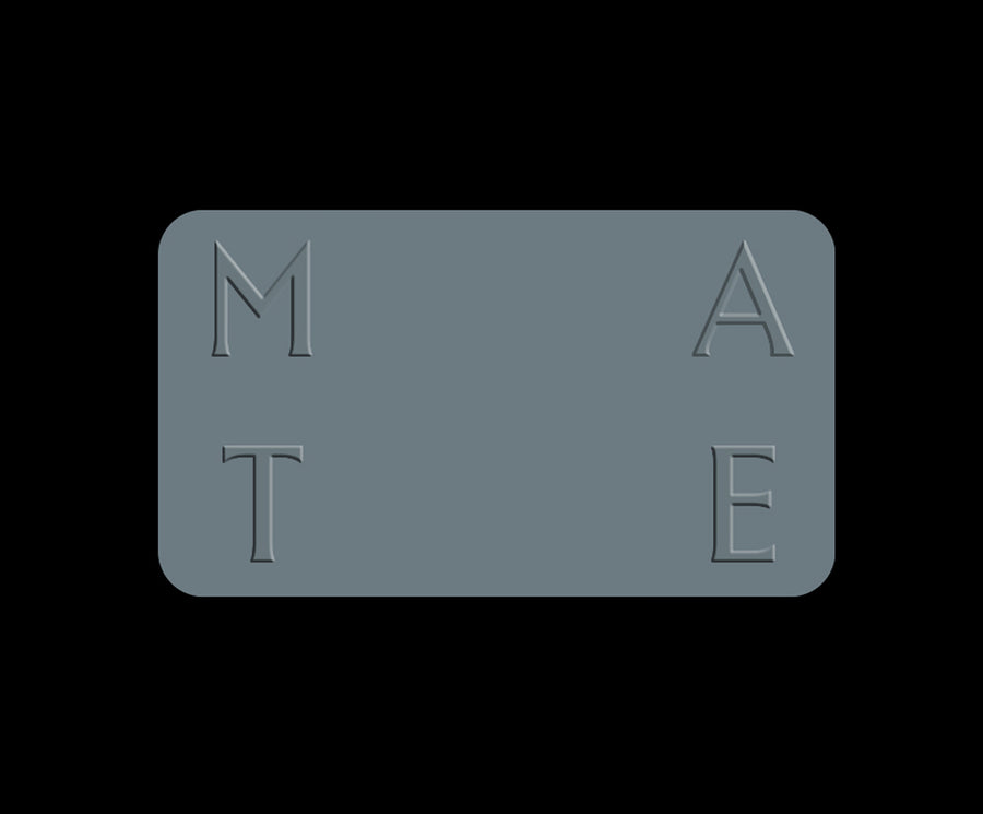 A rectangular slate gray plaque with rounded corners, featuring the embossed letters 'M', 'A', 'T', and 'E' arranged in a 2x2 grid on a solid black background.