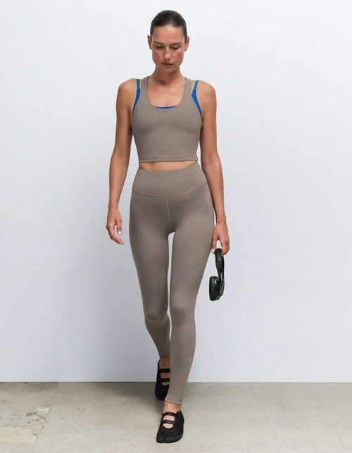 Model wearing a taupe sports bra and matching leggings from Mate the Label, holding a dumbbell