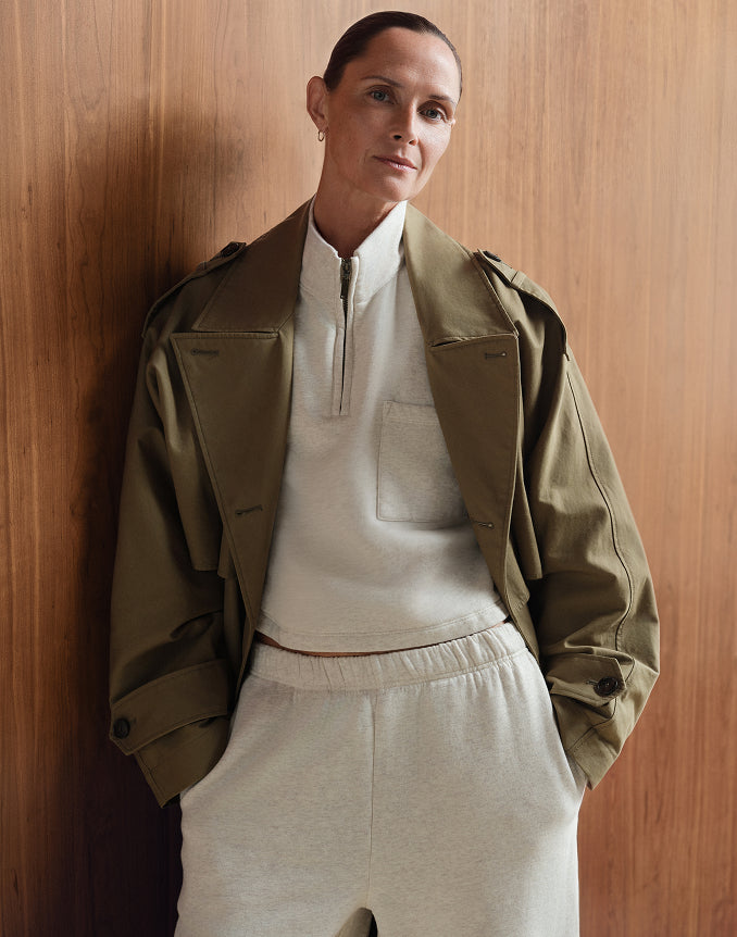 MATE model wearing an olive green cropped jacket over a heather oat quarter-zip top and matching sweatpants, against a wood-paneled wall