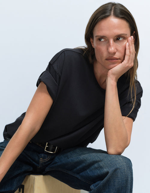 Model wearing a black t-shirt and jeans from Mate the Label, seated