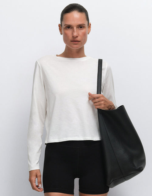 Model wearing a white long-sleeve top and black shorts with a black tote bag, Mate the Label